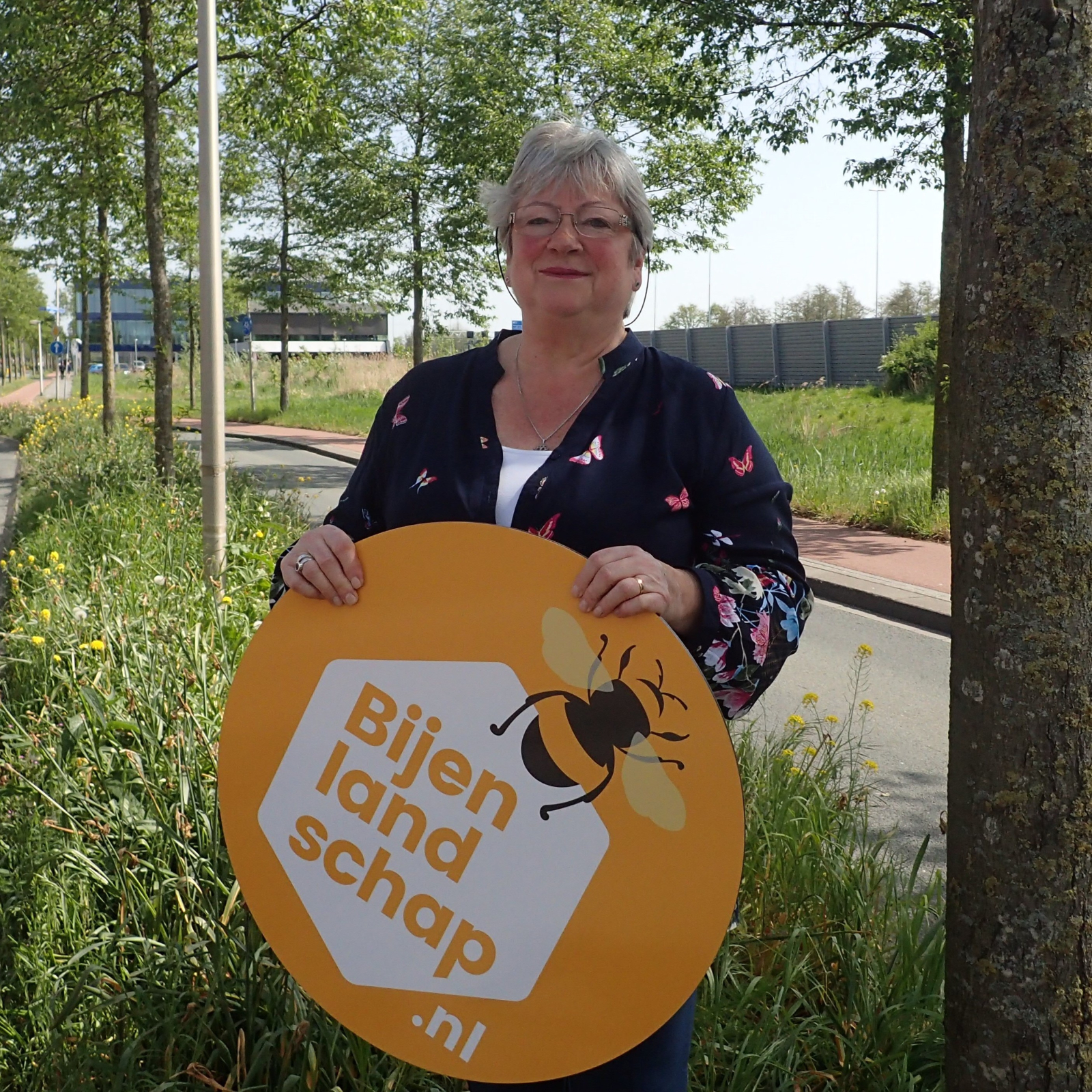 Wilma Gerver met een rond bord waarop het logo van Bijenlandschap staat