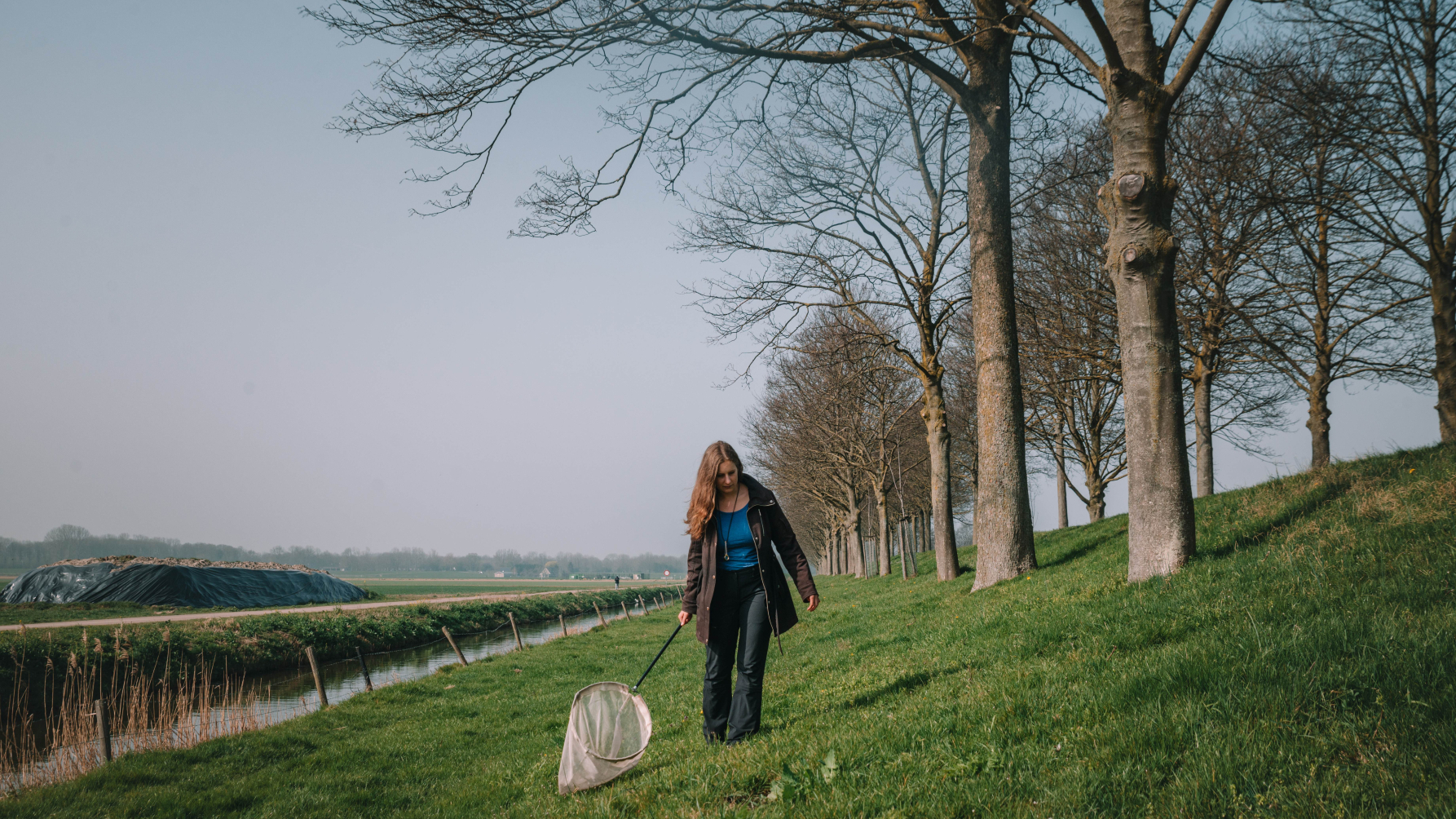 Linde Slikboer met een insectennet op een dijk