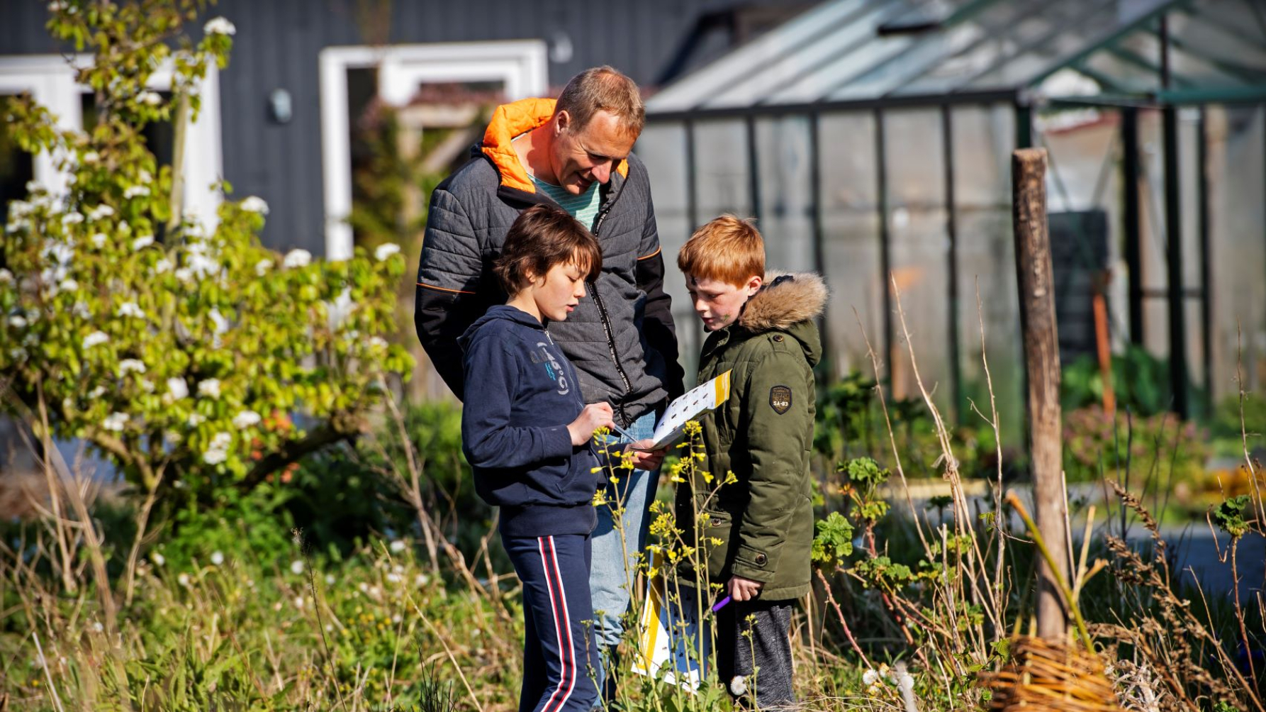 man en twee kinderen met bijengids in de tuin