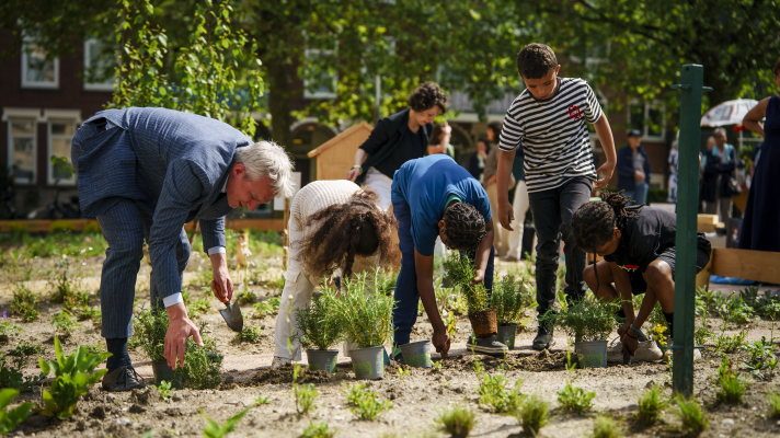Kinderen zetten planten in de grond op het Bospolderplein in Rotterdam, samen met gedeputeerde Berend Potjer